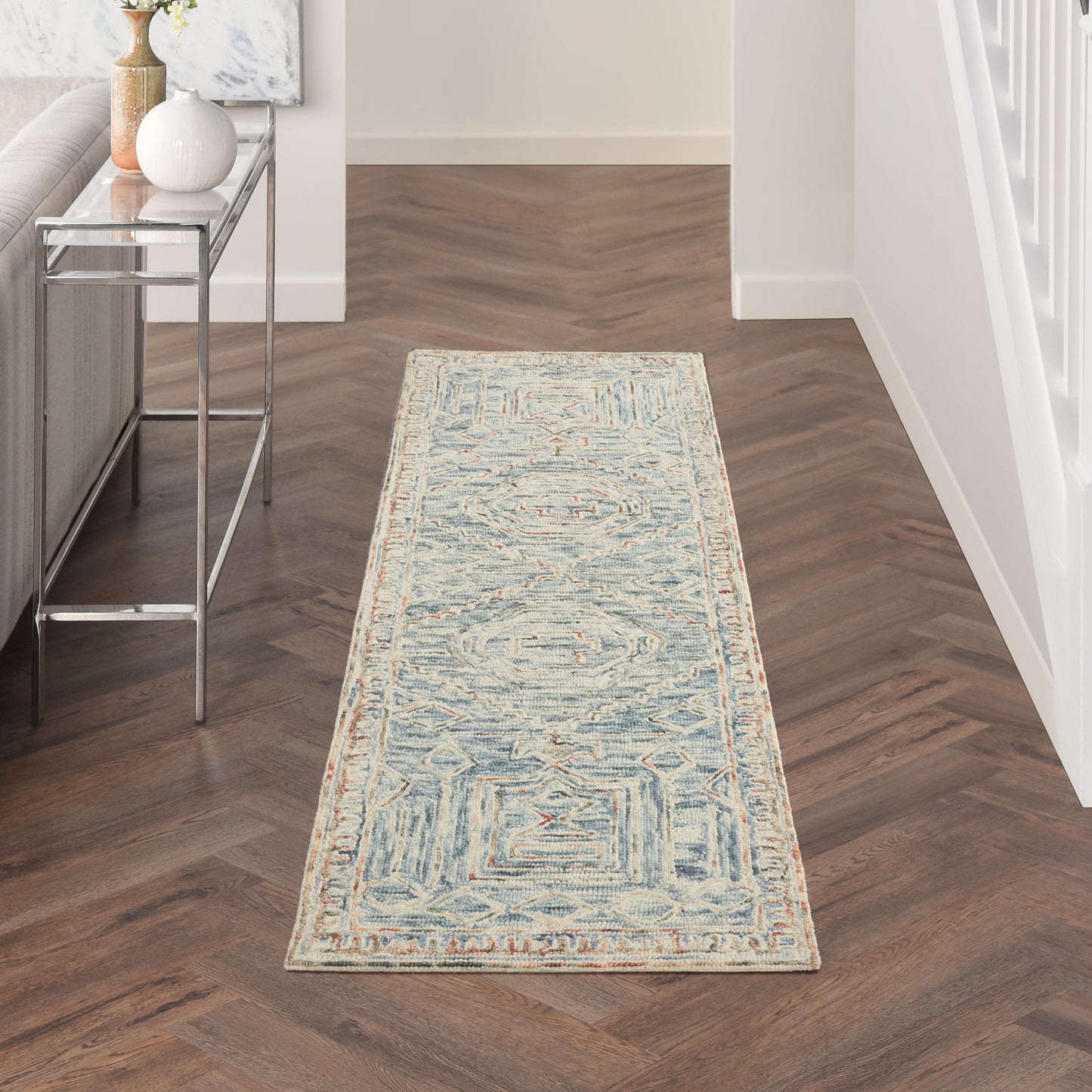 Blue and ivory geometric runner rug in hallway with a light border on dark wood floor.