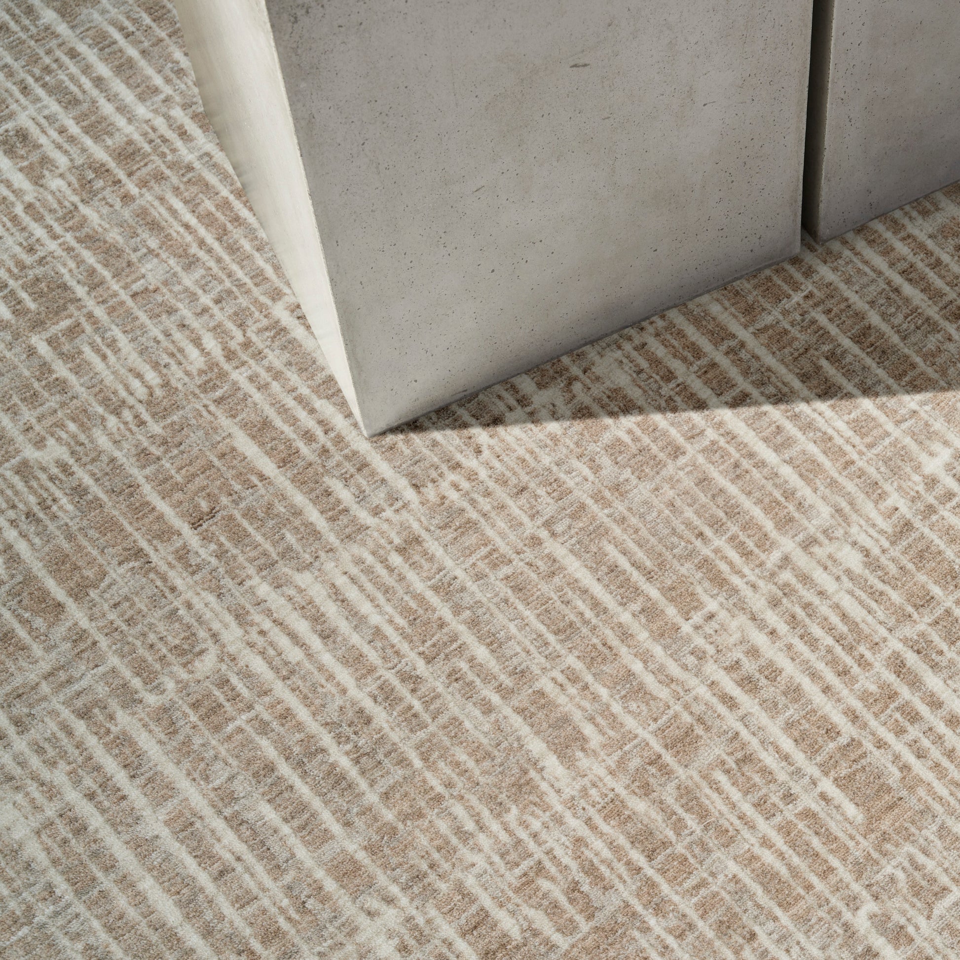 Beige textured carpet with tan linear stripes; corner of a concrete block resting on the rug.