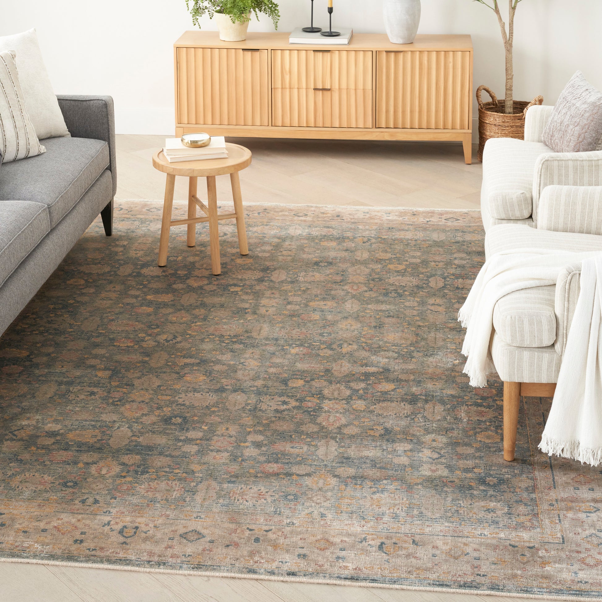 Cozy living room with vintage blue-rust oriental rug, round light wood coffee table, grey sofa, and cream armchairs.