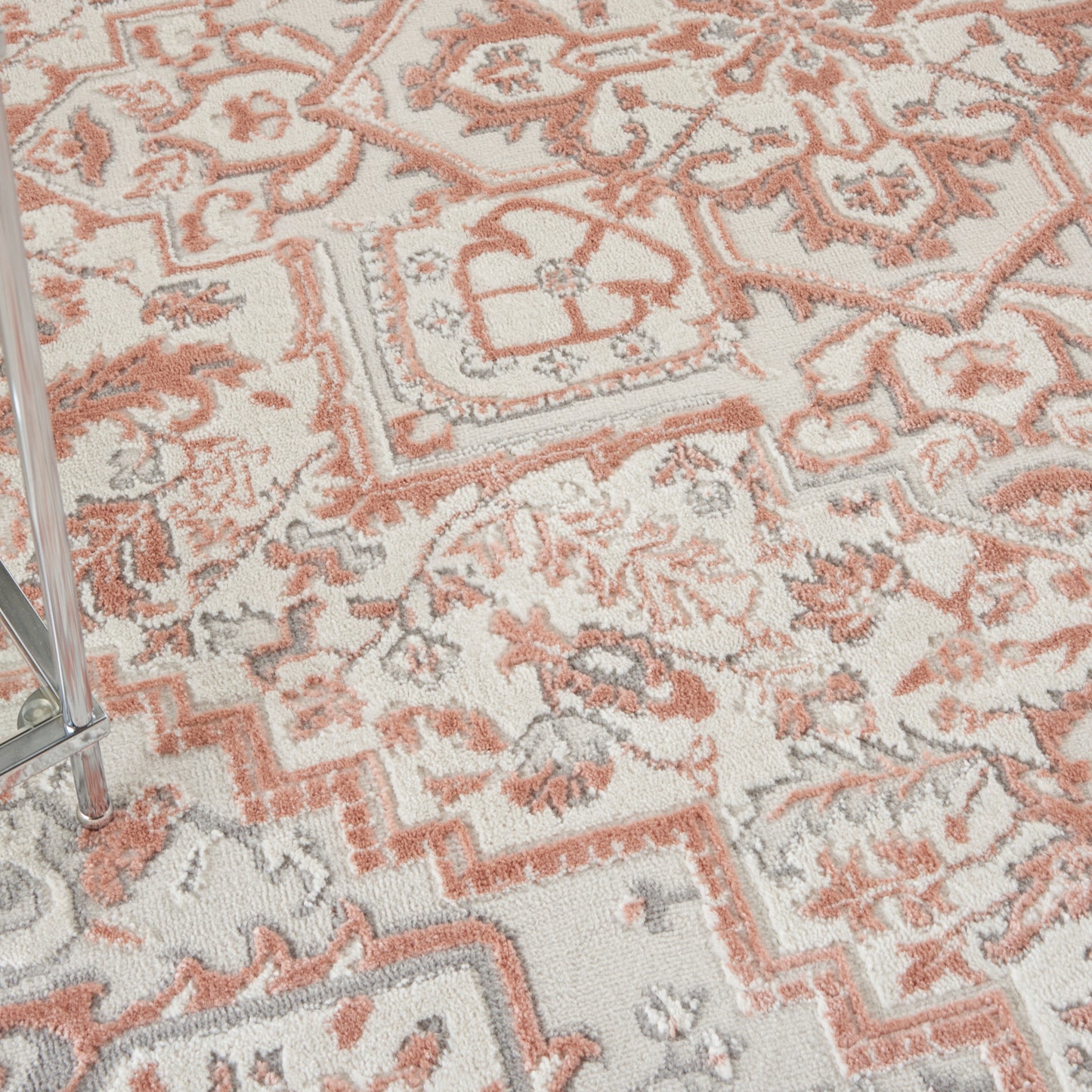 Close-up of oriental rug in coral-orange, ivory and gray with floral pattern and zigzag border; chrome chair leg.