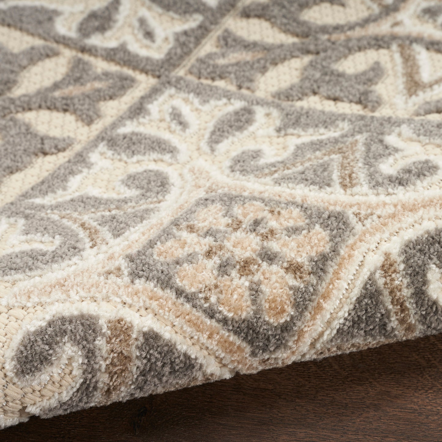 Close-up of a plush gray and cream patterned rug with ivory scroll motifs on a wooden floor.