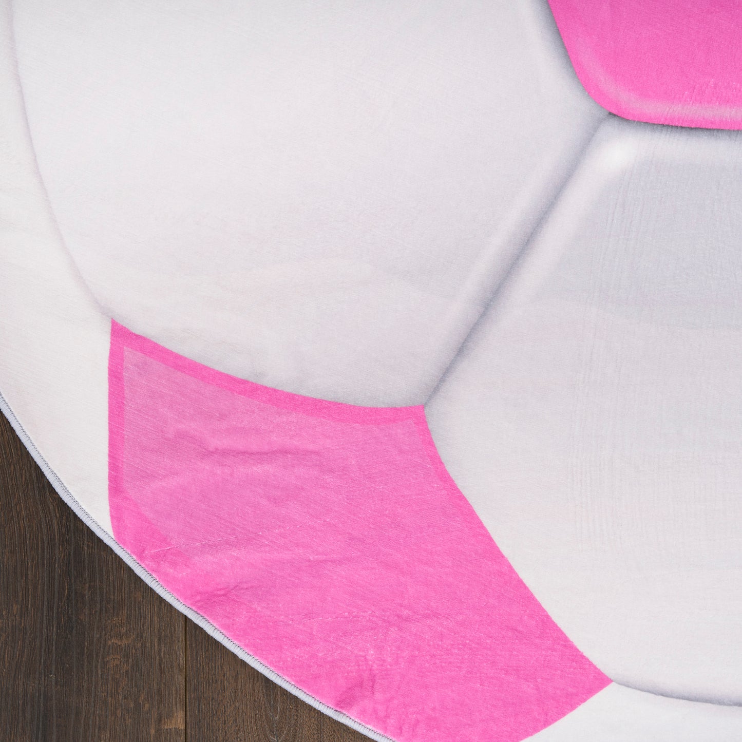 Round pink and white patchwork cushion on dark wood floor, quilted fabric.