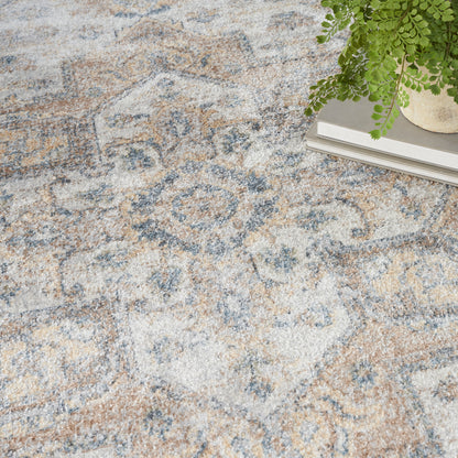 Patterned ivory and blue area rug with tan accents; a green fern sits atop a stack of books.