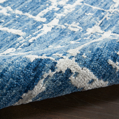 Close-up of blue rug with white abstract pattern; plush textured pile and folded edge.