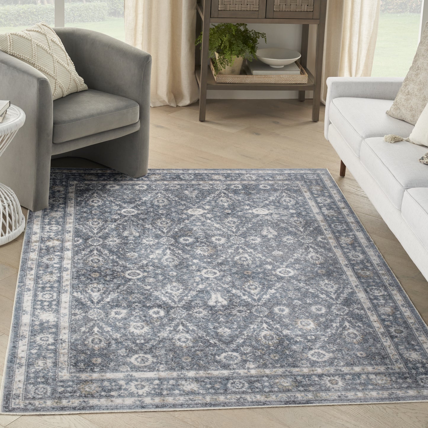 Blue-gray oriental rug with ivory motif and border, in a bright living room with gray chair and white sofa.