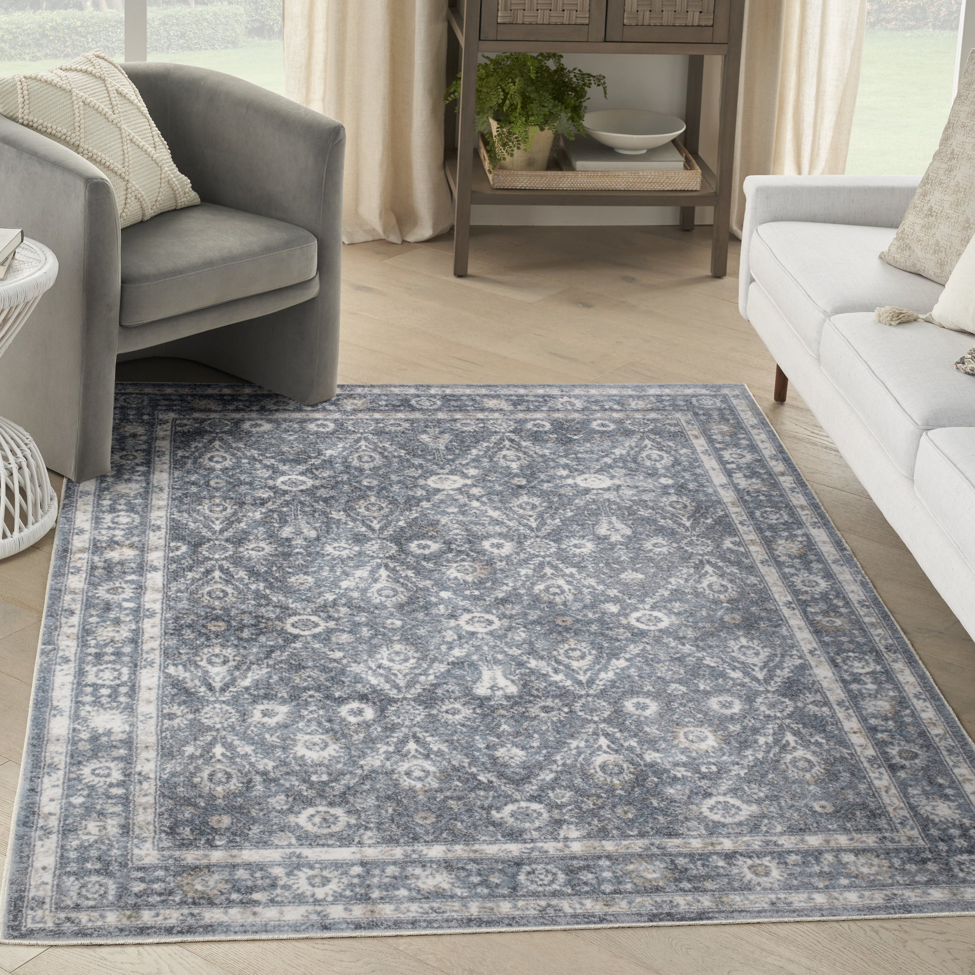 Blue-gray oriental rug with ivory motif and border, in a bright living room with gray chair and white sofa.