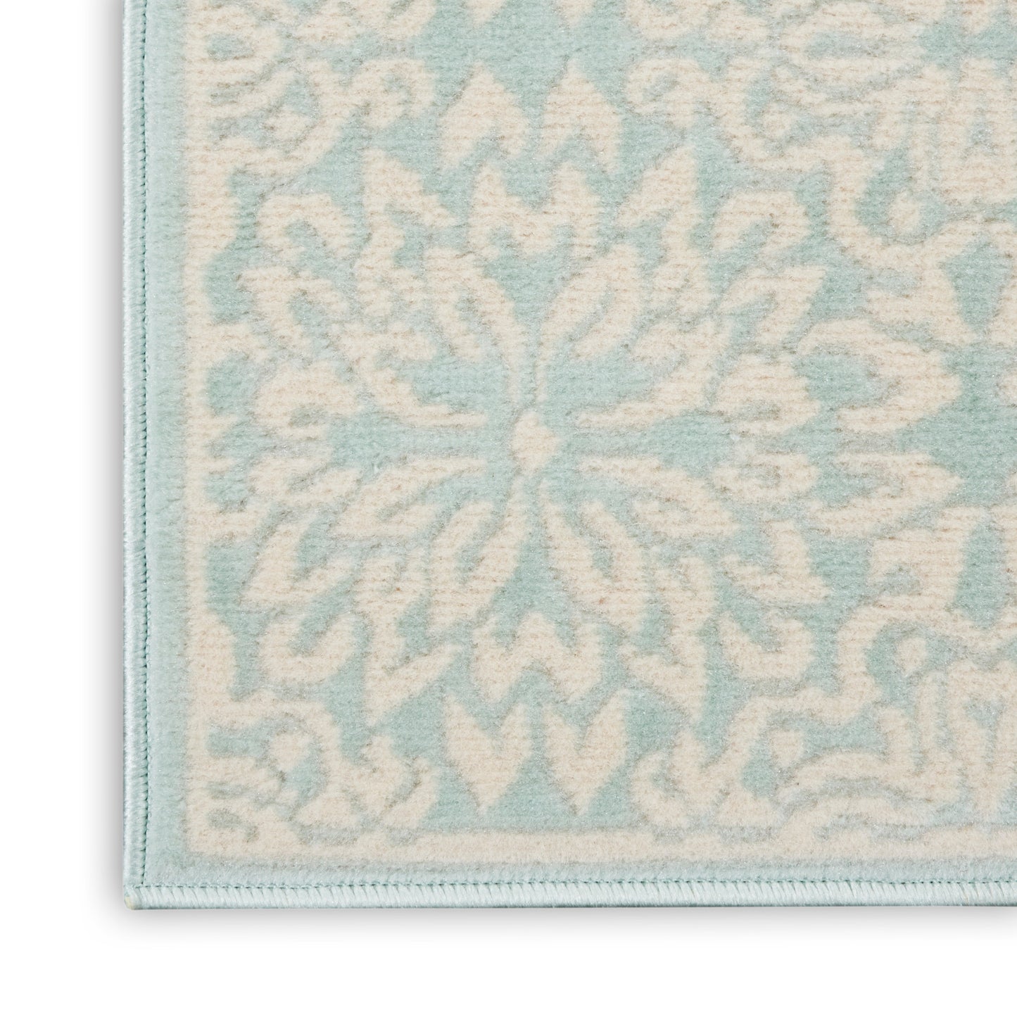 Close-up of pale blue and ivory damask rug with a light blue border and textured floral motif.