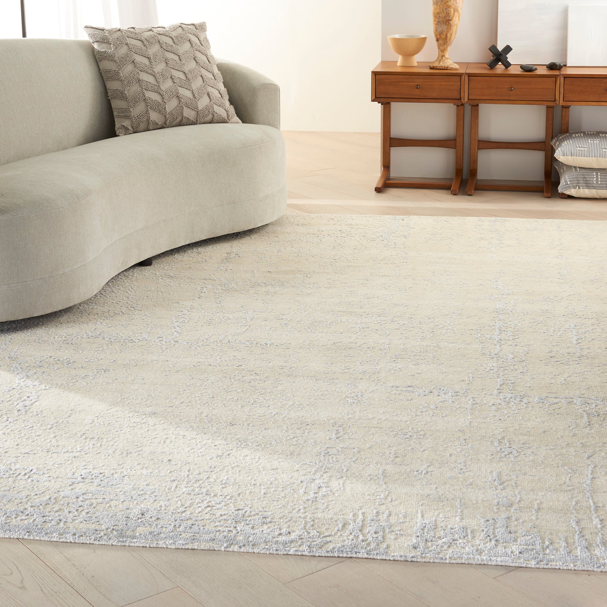 Cream textured area rug with subtle pattern on light wood floor beside a curved gray sofa and wooden console with decor.