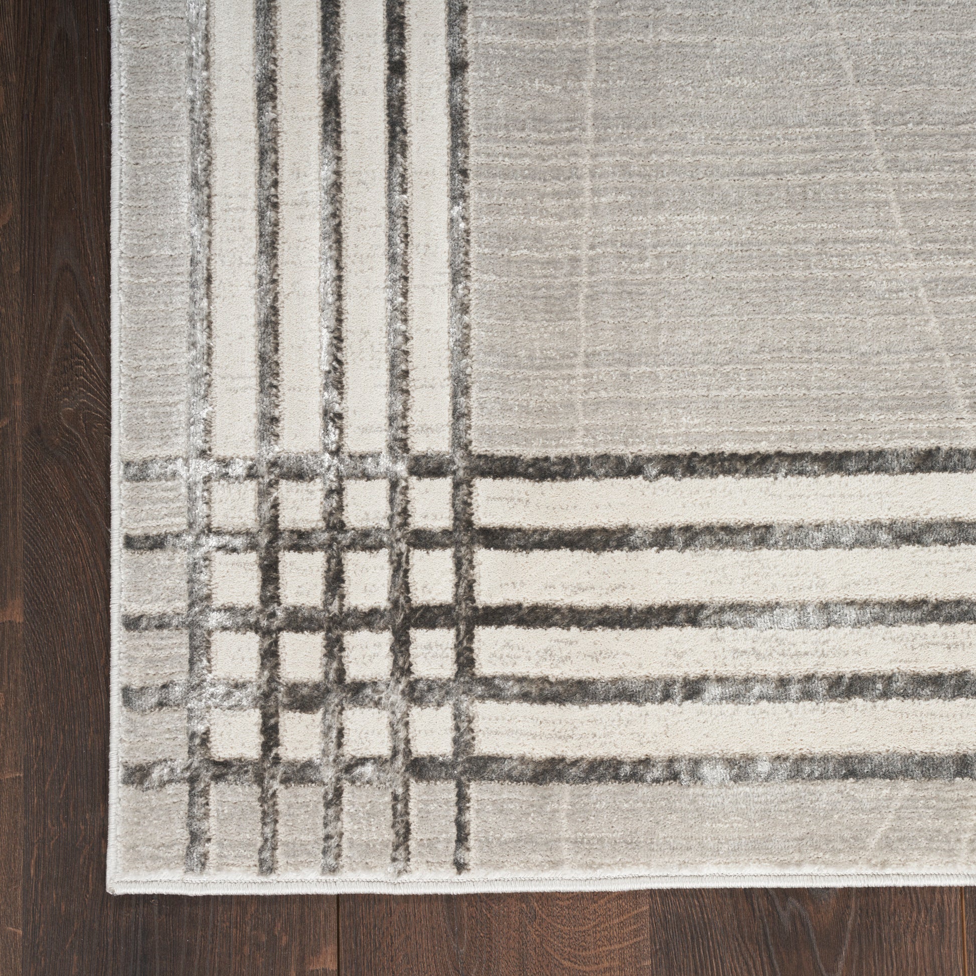 Light gray area rug with dark charcoal grid lines and square corner motif on dark wood floor.