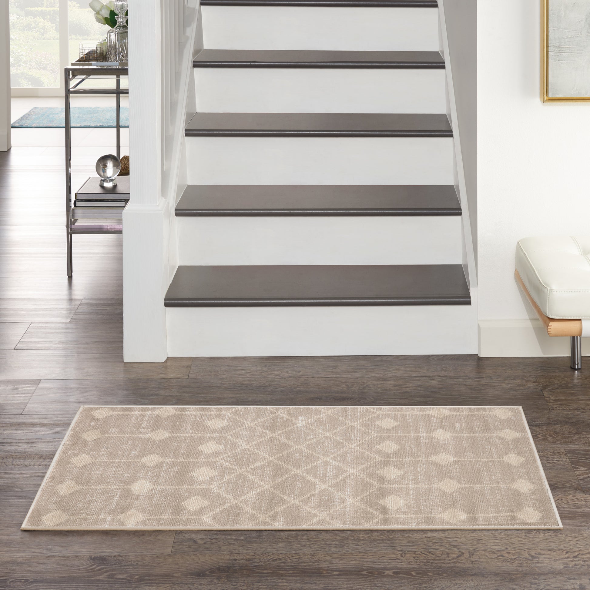 Beige geometric area rug on dark hardwood floor in front of a white staircase with dark brown treads.