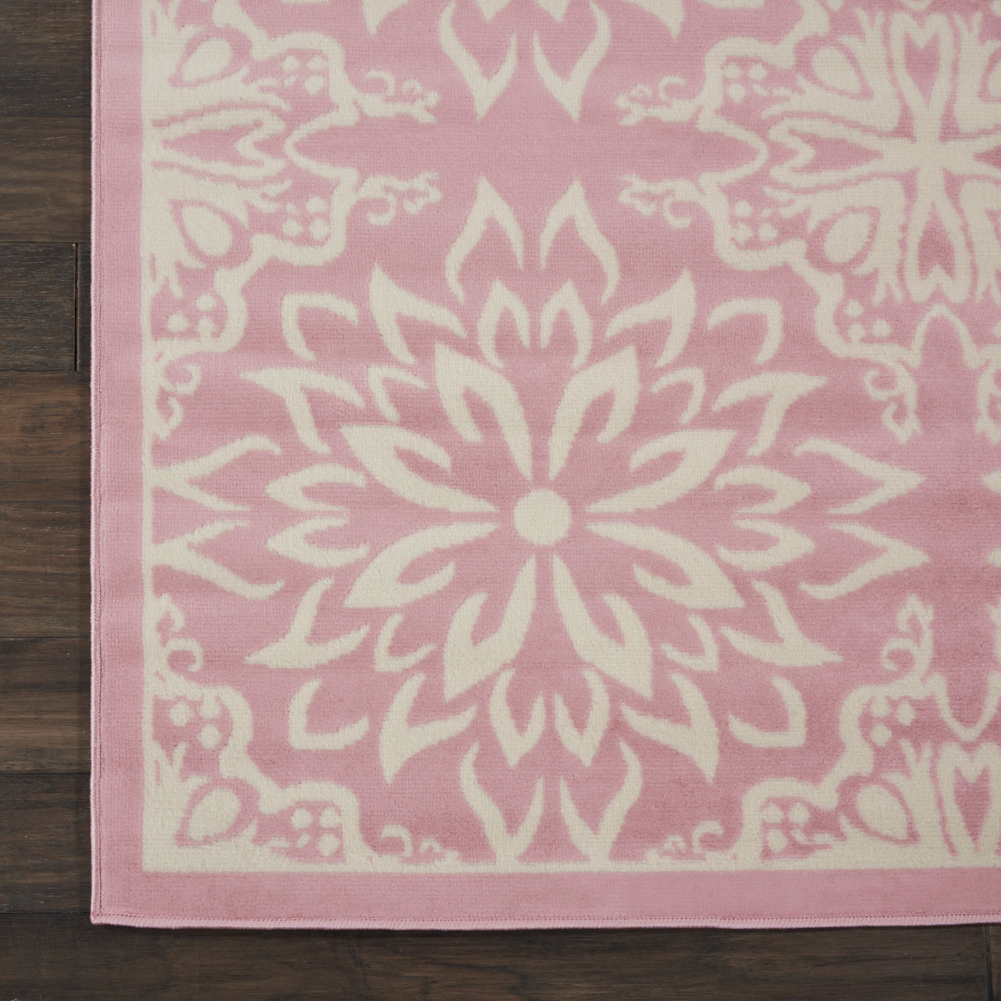 Pink and cream rug with a large central mandala floral pattern and pink border on a dark wooden floor.