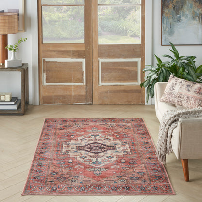 Persian-style red area rug with blue and ivory borders on light wood floor, beside beige sofa and houseplant.