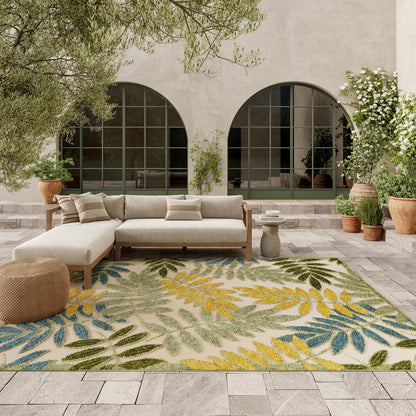 Outdoor courtyard seating with beige sectional sofa, tropical leaf rug in blue/green/yellow, potted plants & arched windows.