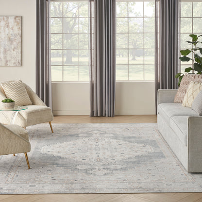 Neutral living room with beige woven chair, glass side table, gray sofa, blue-gray patterned rug, and dark gray curtains.