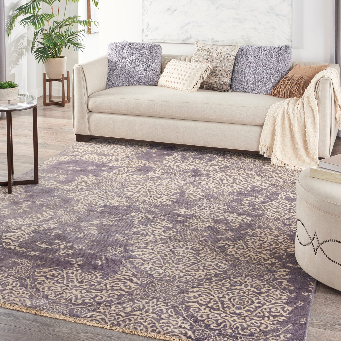 Purple and taupe ornate area rug in a light living room with a beige fabric sofa and plush throws
