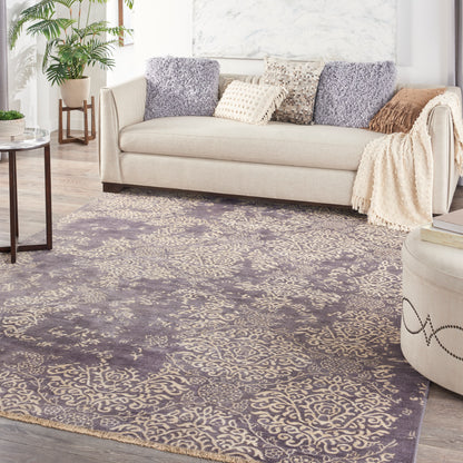 Purple and taupe ornate area rug in a light living room with a beige fabric sofa and plush throws
