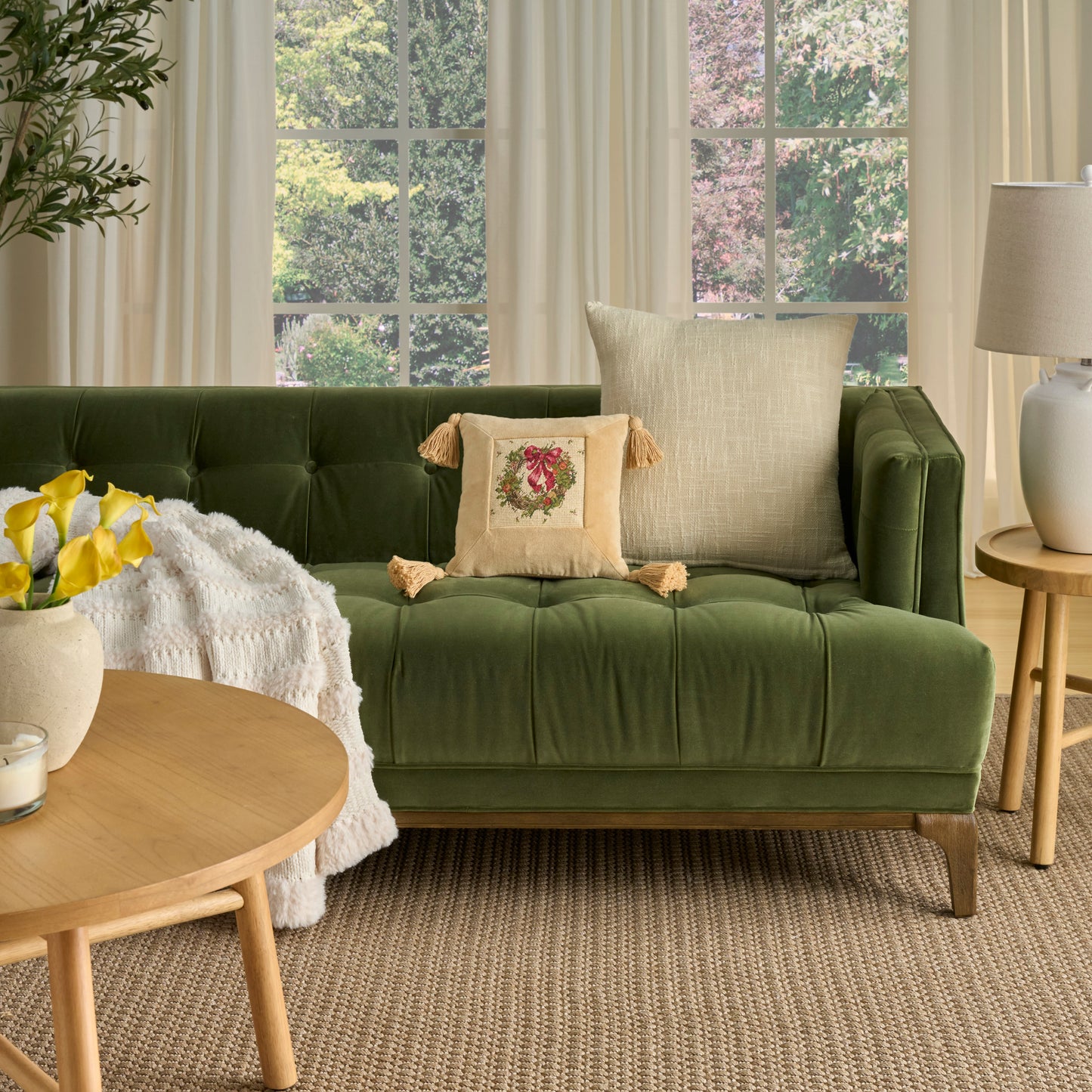 Green tufted velvet sofa with beige tassel pillow, large neutral cushion, cream throw, round wooden coffee table.