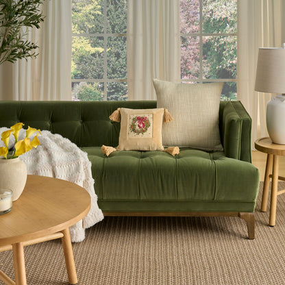 Green tufted velvet sofa with beige tassel pillow, large neutral cushion, cream throw, round wooden coffee table.