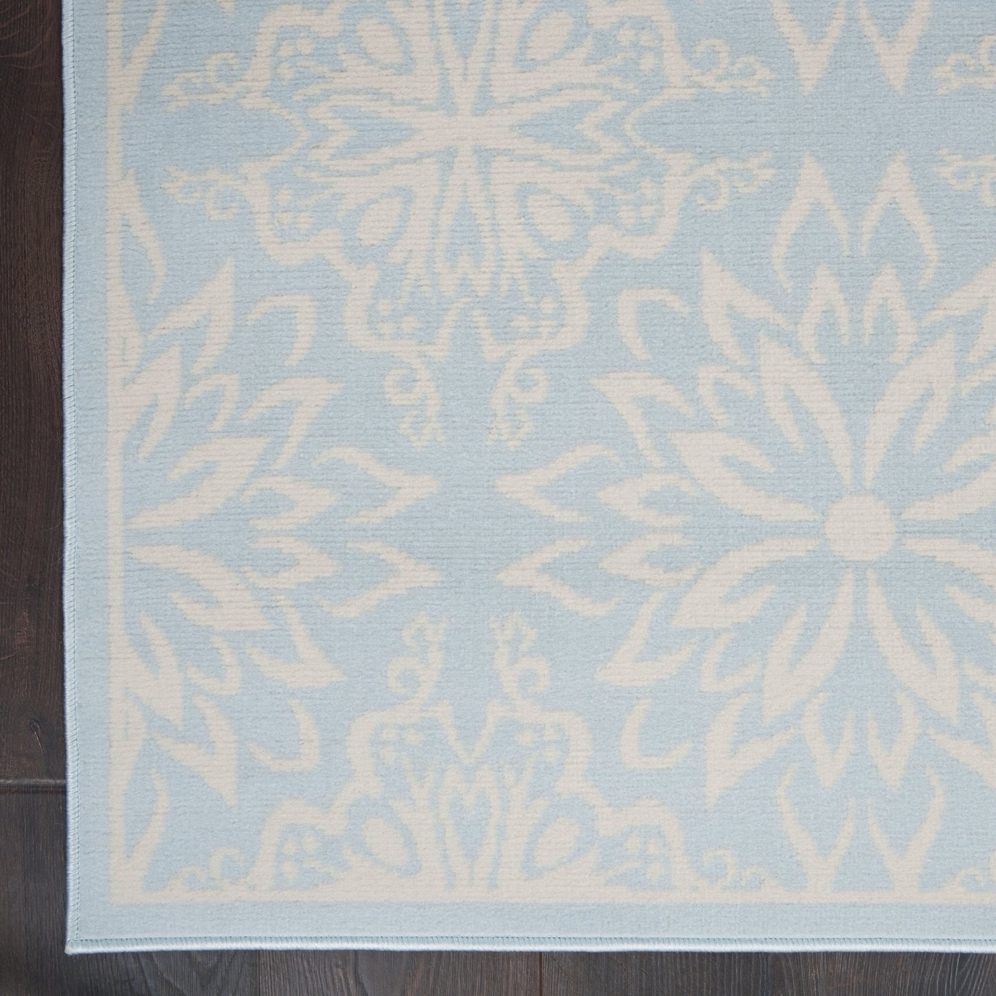 Rectangular light-blue rug with white snowflake floral motifs and pale blue border; woven textile for living spaces.