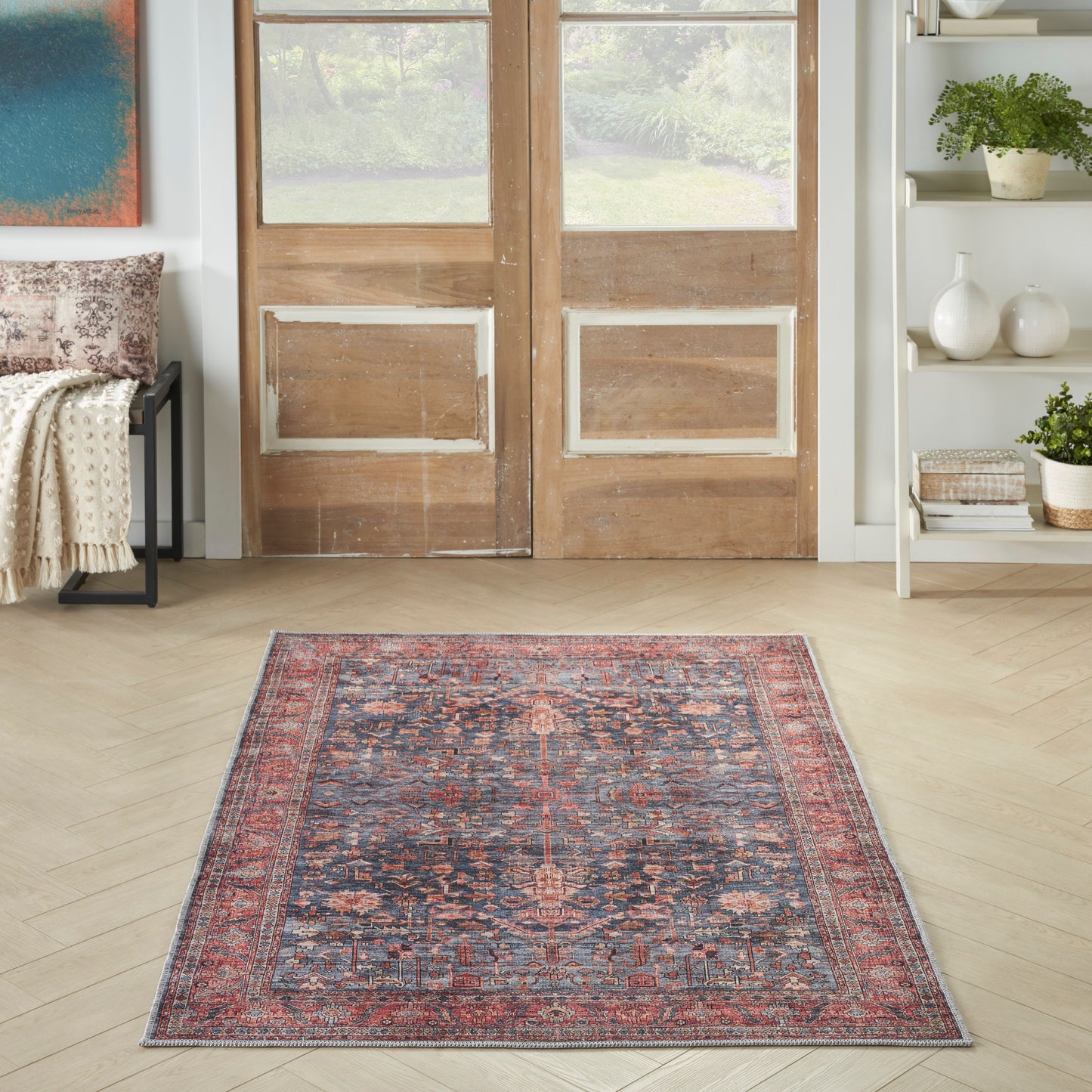 Rectangular Persian-style area rug with red, navy and ivory floral motifs, placed on a light wood floor in front of wooden doors.