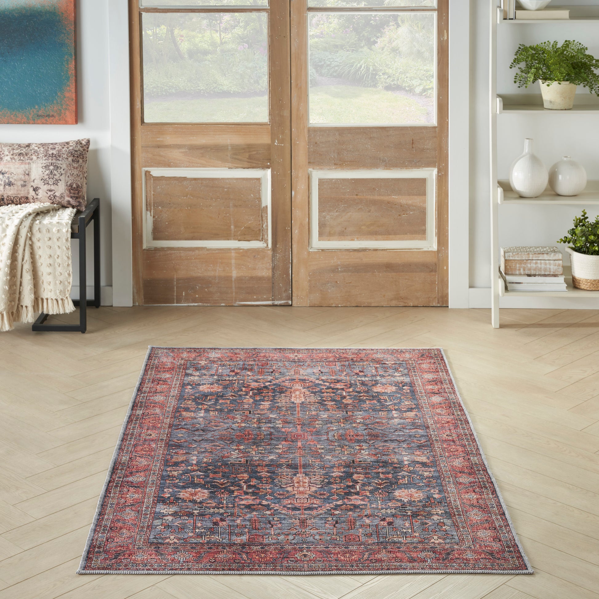 Rectangular Persian-style area rug with red, navy and ivory floral motifs, placed on a light wood floor in front of wooden doors.