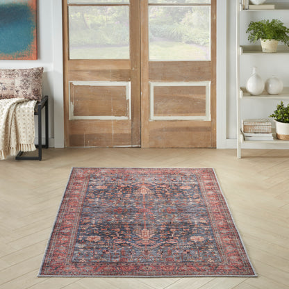 Rectangular Persian-style area rug with red, navy and ivory floral motifs, placed on a light wood floor in front of wooden doors.