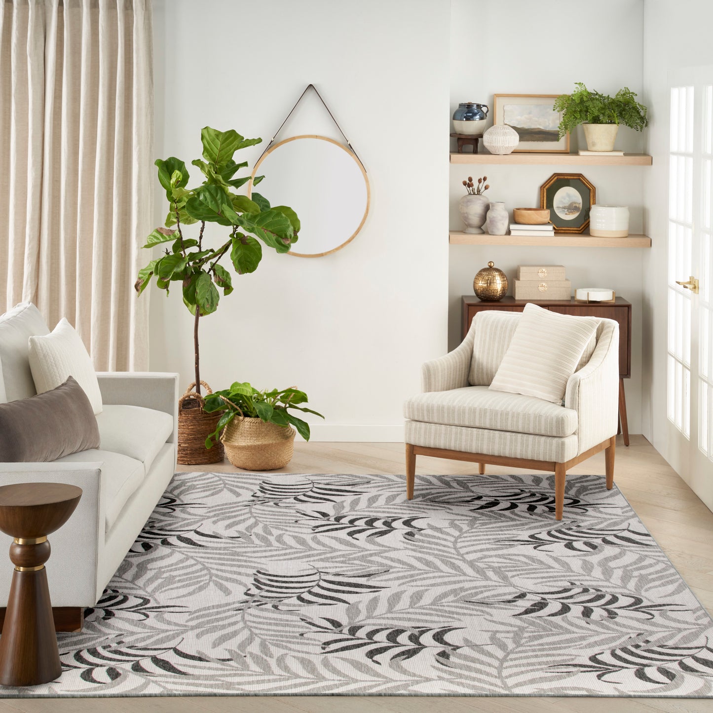 Neutral living room with beige sofa, striped chair, leaf-pattern rug, tall fiddle-leaf fig in wicker basket, round wall hoop.
