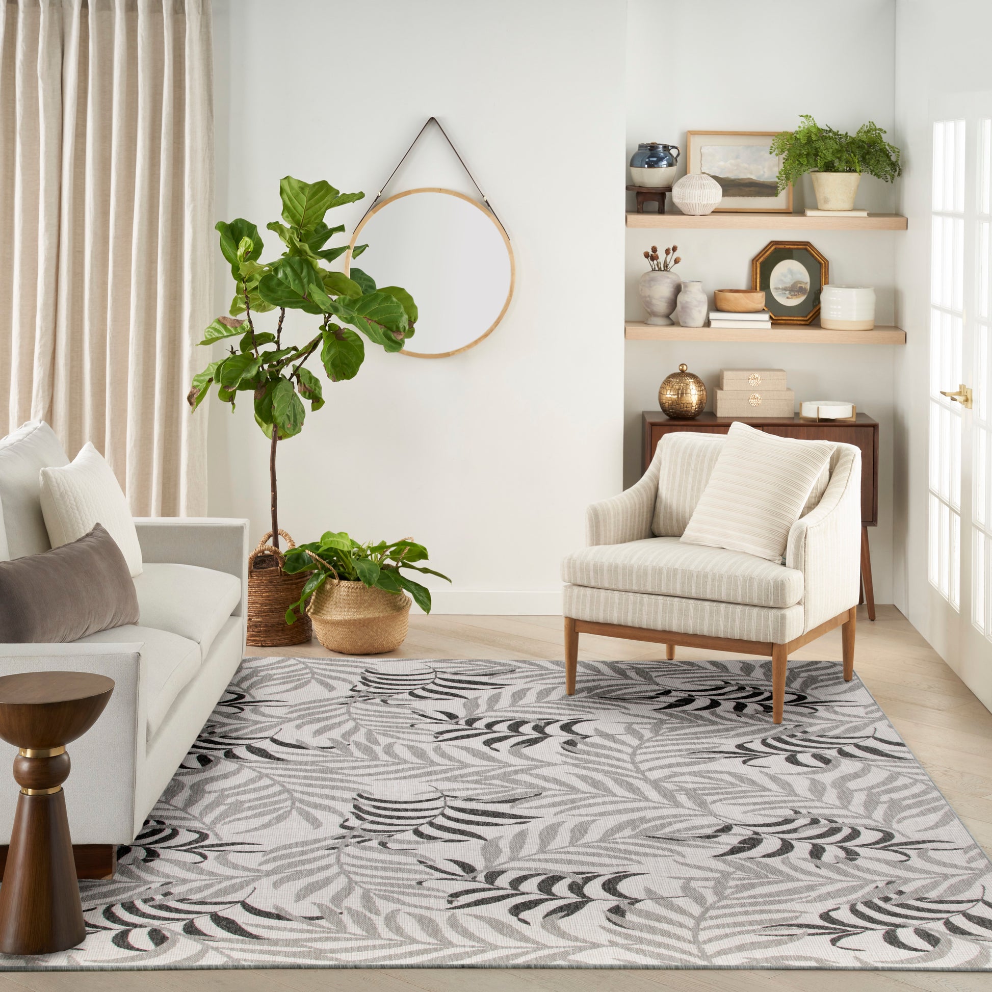 Neutral living room with beige sofa, striped chair, leaf-pattern rug, tall fiddle-leaf fig in wicker basket, round wall hoop.