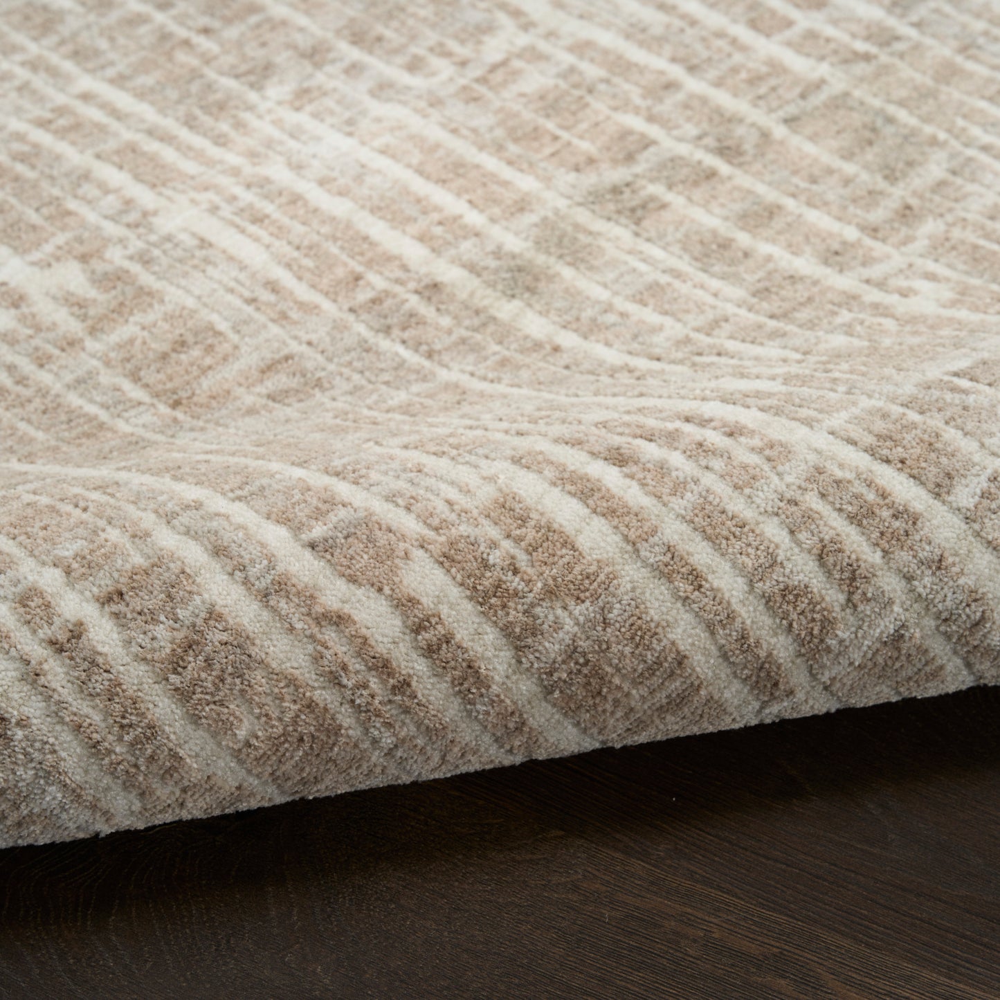 Beige textured rug with a wavy geometric pattern and plush pile on dark wood floor.