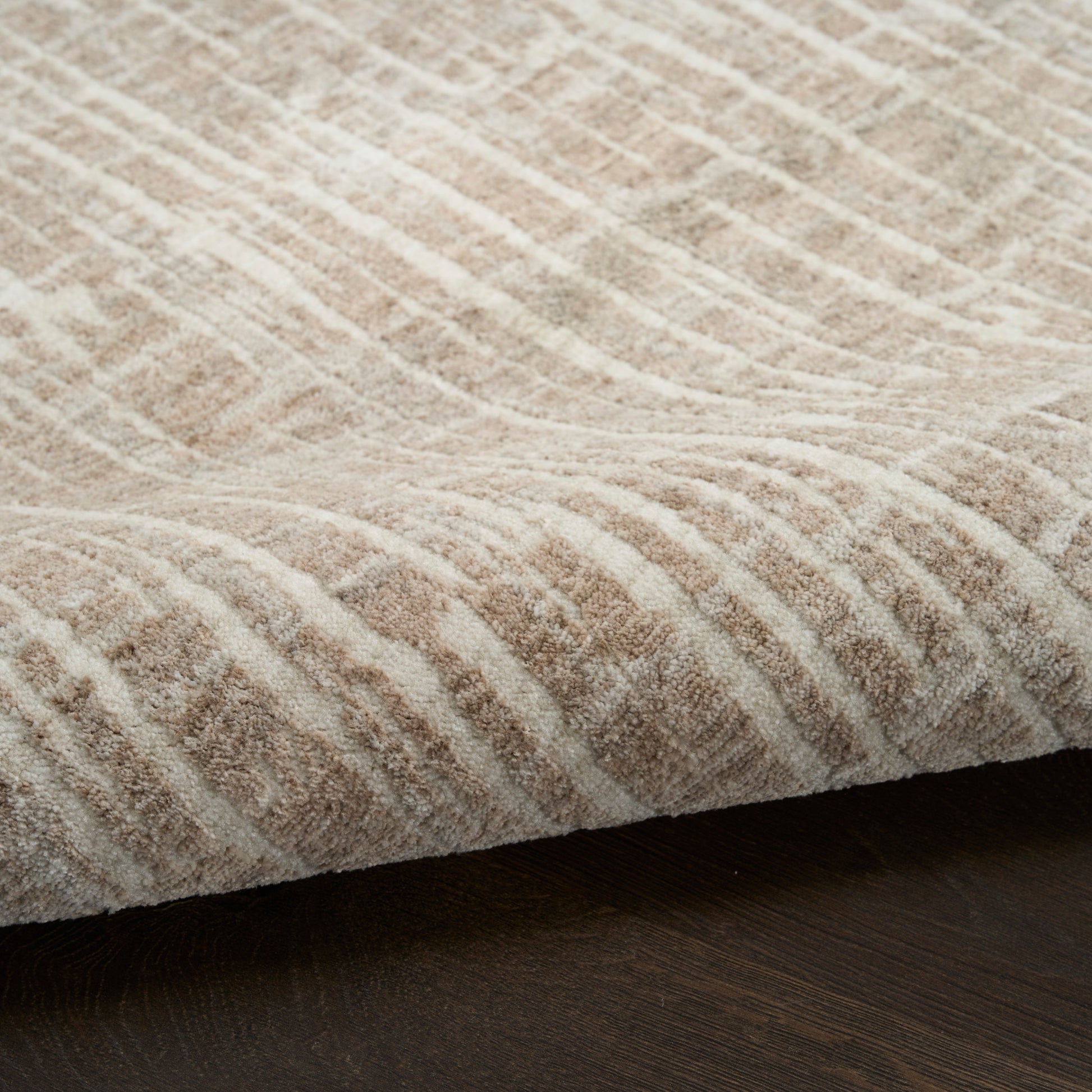 Beige textured rug with a wavy geometric pattern and plush pile on dark wood floor.