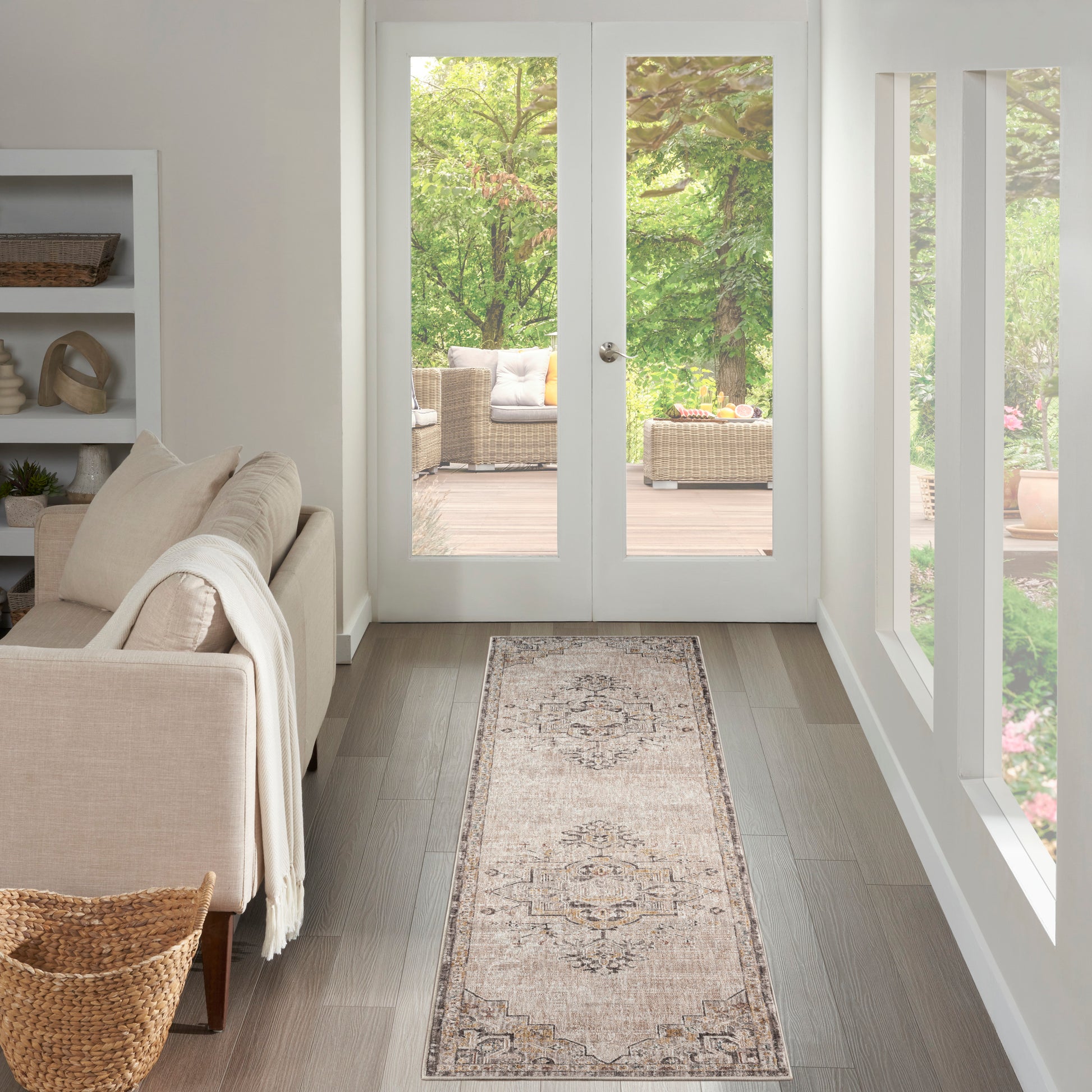 Bright living room with beige sofa, white throws, woven basket, light wood floor, runner rug, and French doors to garden.
