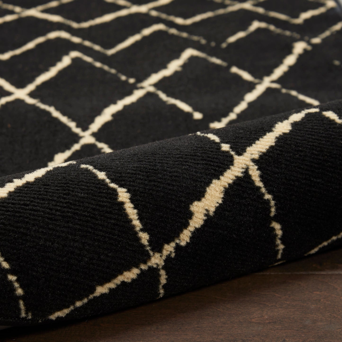 Black rug with cream geometric diamond lattice pattern; plush woven pile.