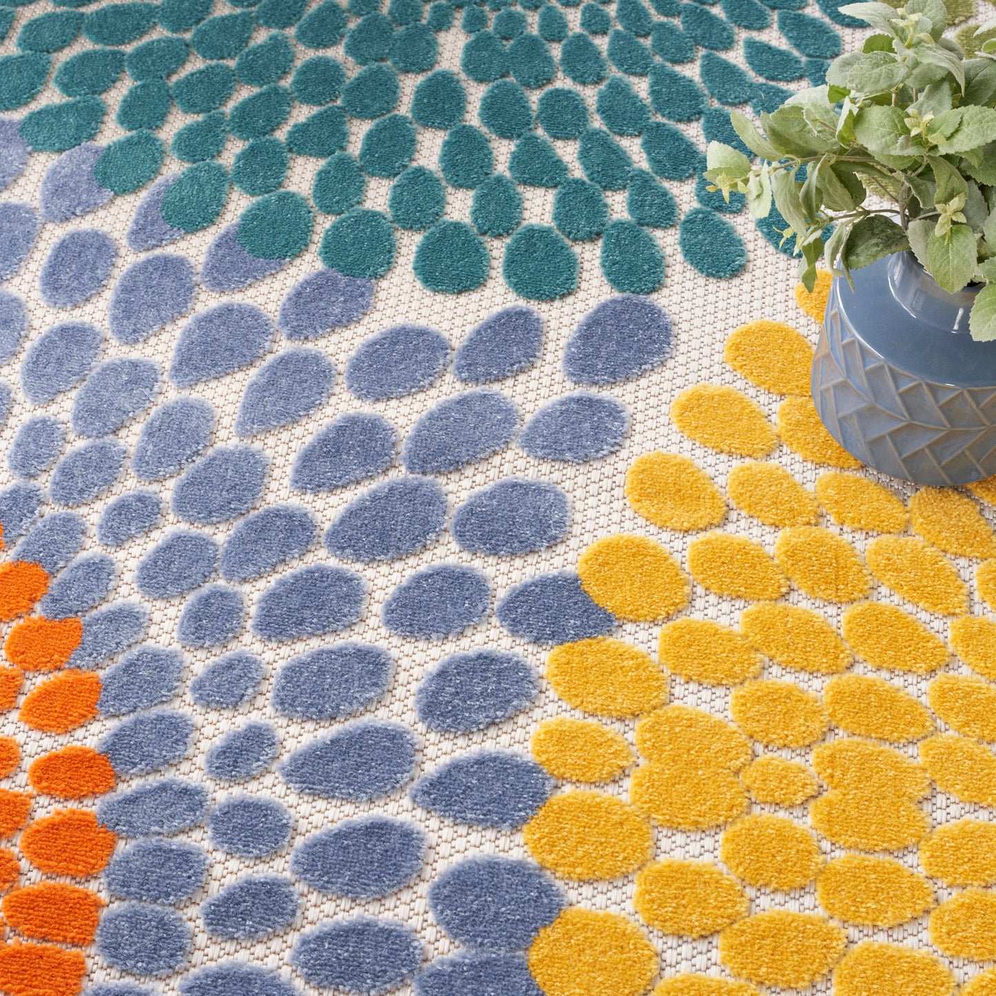 Colorful tufted rug with teal-green, blue and yellow circular dots; plant in a gray geometric pot on the edge.
