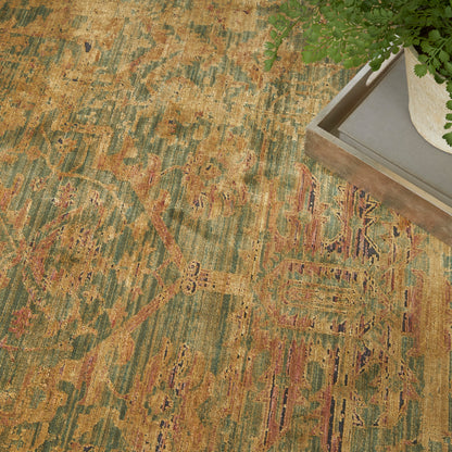 Vintage oriental rug in olive, gold & rust tones with distressed pattern; wooden tray & greenery in corner.