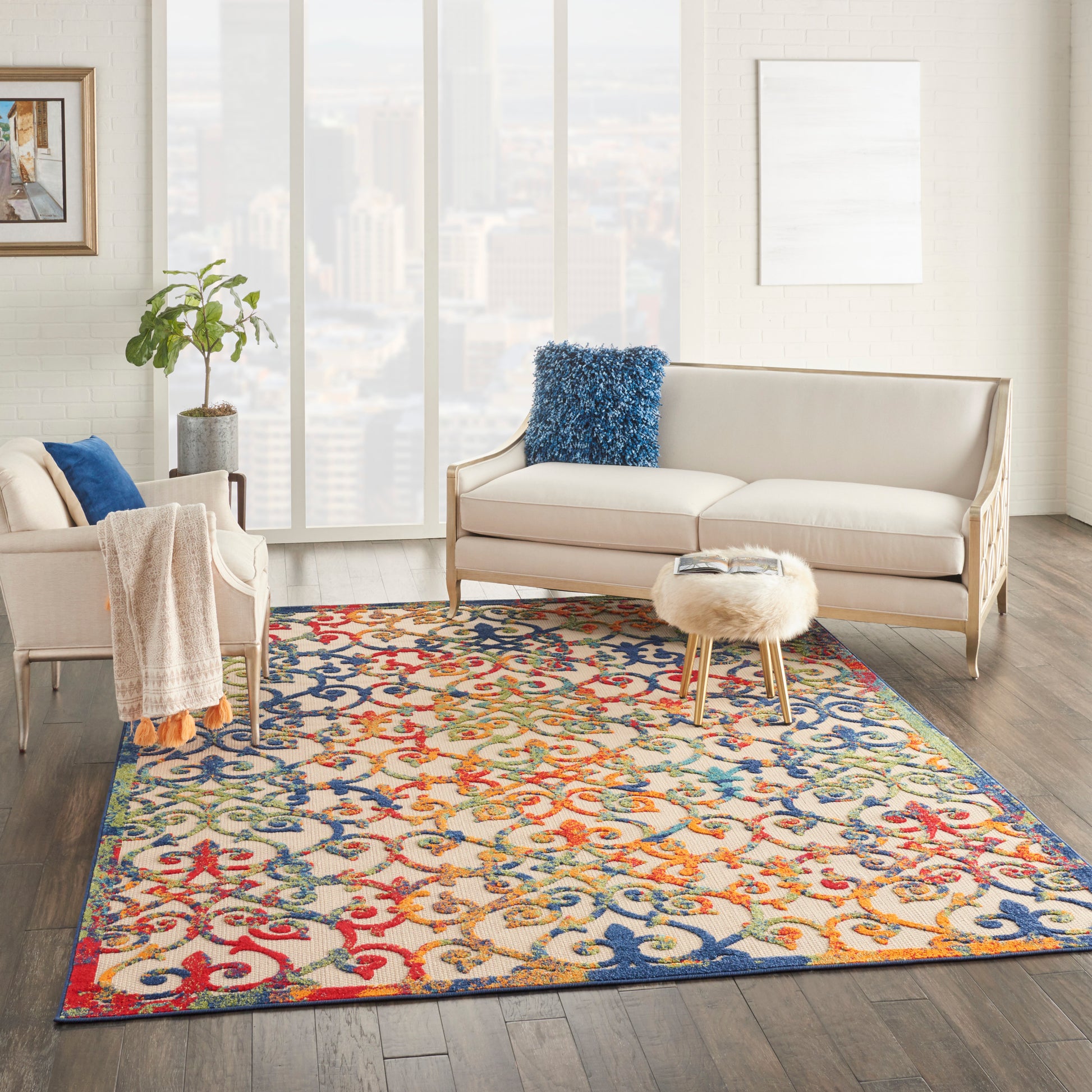 Bright living room with cream sofa and chair, vibrant ornate rug, round faux-fur ottoman, blue throw pillow.