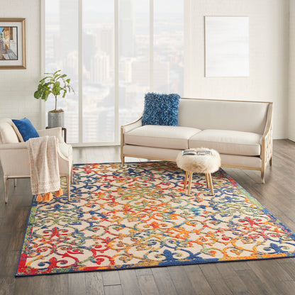 Bright living room with cream sofa and chair, vibrant ornate rug, round faux-fur ottoman, blue throw pillow.