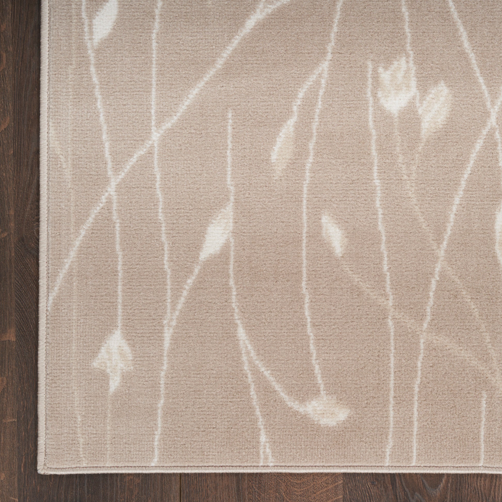Beige area rug with white abstract branch pattern on dark wood floor; modern, soft woven look.