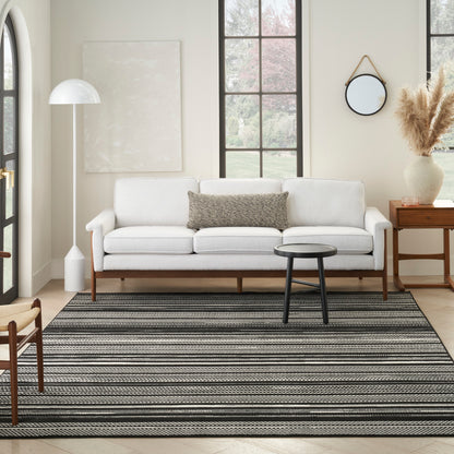 Bright living room with white sofa, gray cushion, black round coffee table, striped grey-black rug, floor lamp, pampas vase.