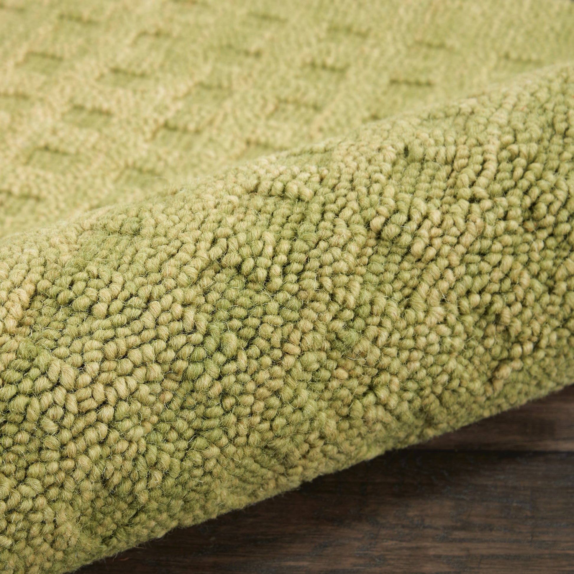 Olive-green shaggy rug close-up with dense looped pile on dark wooden floor.