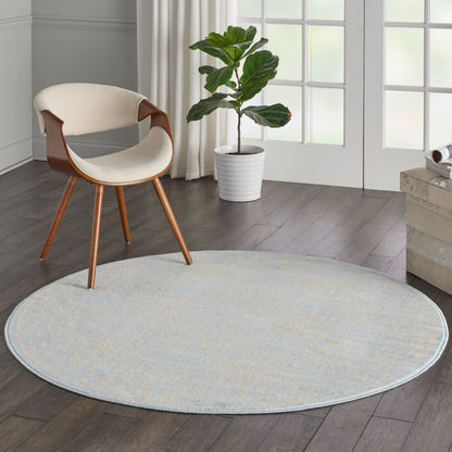 Round pale blue rug on a wood floor with a cream curved-seat chair and wooden legs beside a tall plant in a white pot.