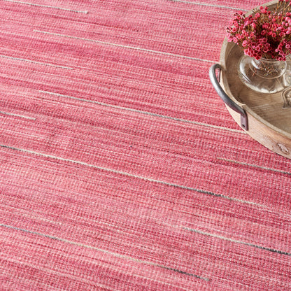 Pink striped woven rug with a round wooden tray holding a glass vase of pink flowers.
