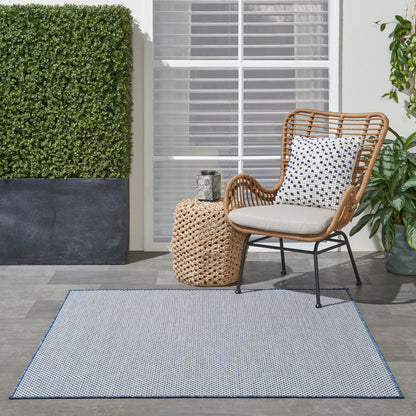 Outdoor patio: wicker chair with beige cushion and blue-white patterned pillow, round woven side table and blue patterned rug