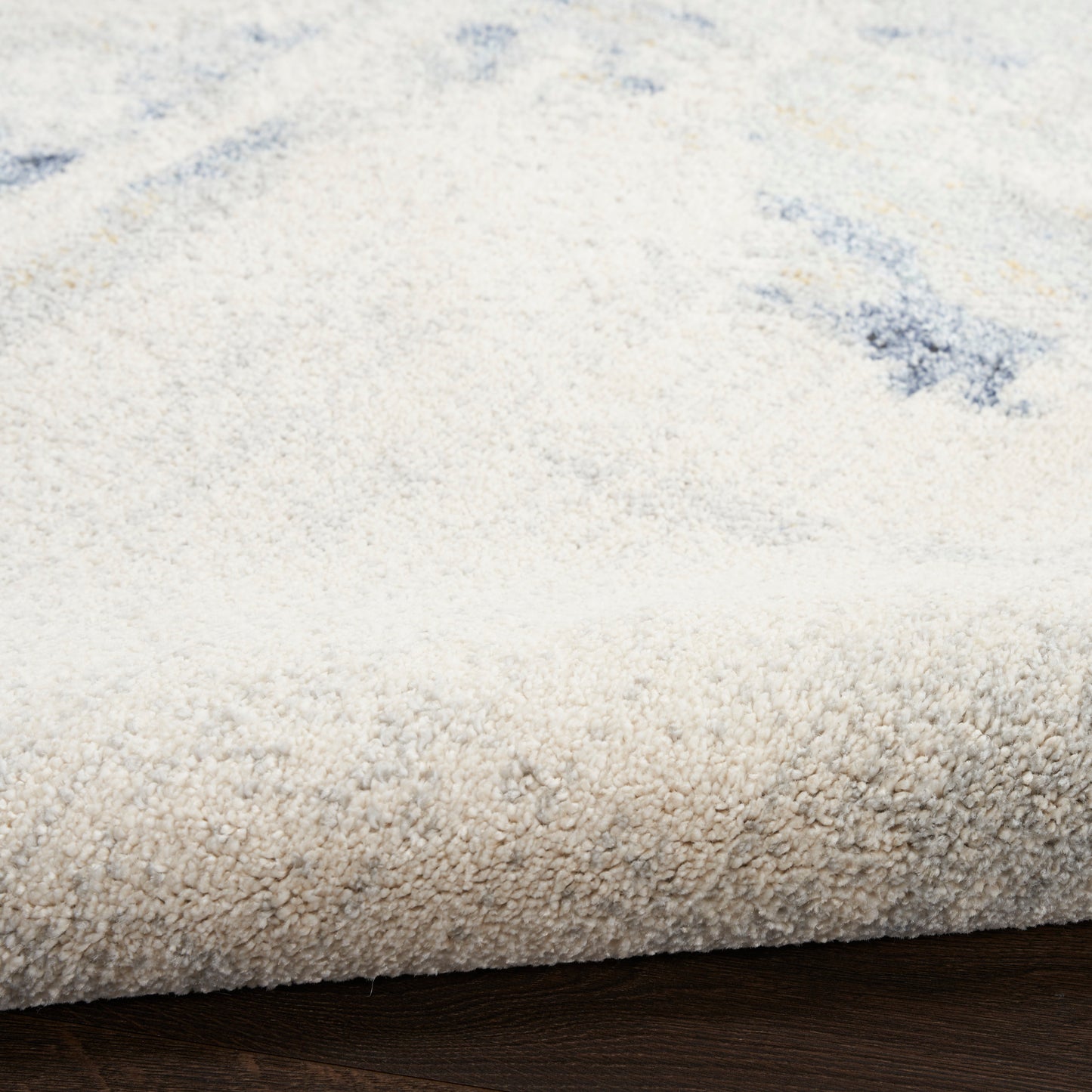 Cream shag rug with plush pile and subtle blue accents; rolled edge on dark wood floor.