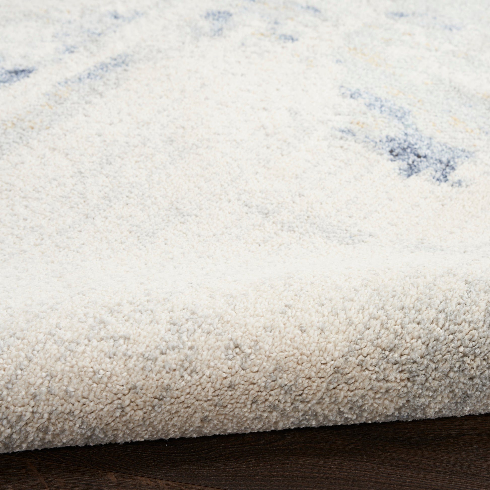 Cream shag rug with plush pile and subtle blue accents; rolled edge on dark wood floor.
