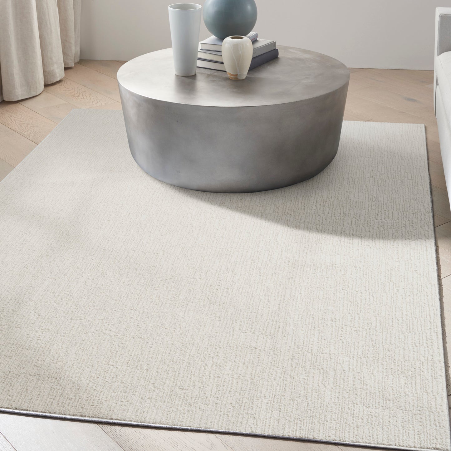 Round concrete coffee table with vases and books on a light beige textured rug in a modern minimalist living room.