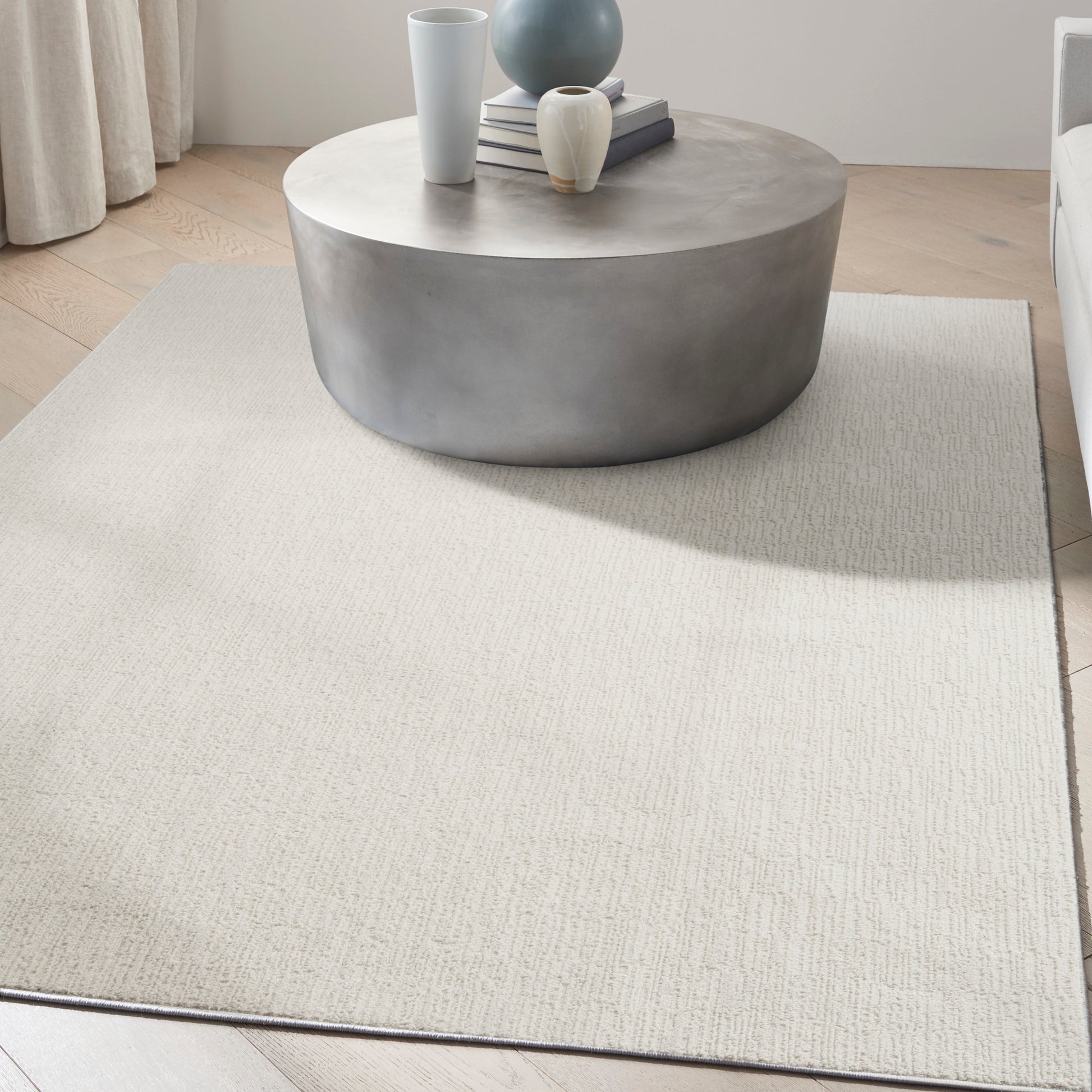 Round concrete coffee table with vases and books on a light beige textured rug in a modern minimalist living room.