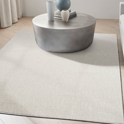 Round concrete coffee table with vases and books on a light beige textured rug in a modern minimalist living room.