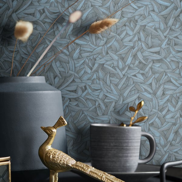 Blue-gray matte vase with dried grasses, a dark mug on a saucer, and a gold peacock figurine against leaf-patterned wallpaper.