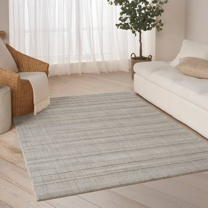 Rectangular light gray striped area rug in a bright living room with white sofa, wicker chair, & potted plant.
