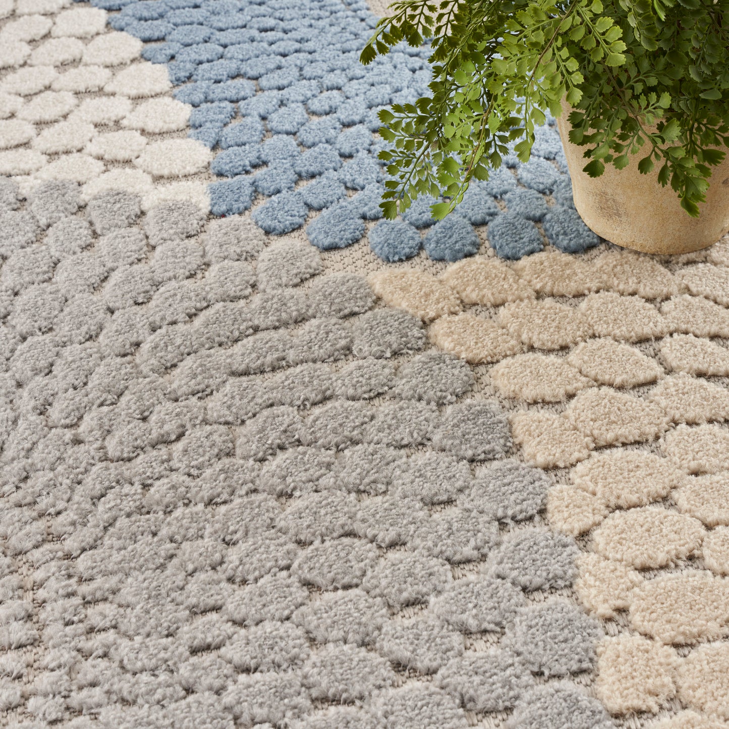 Soft textured rug with circular tufted dots in gray, beige and blue; a potted plant sits at the corner.